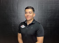 a man in a black polo standing in front of a black background